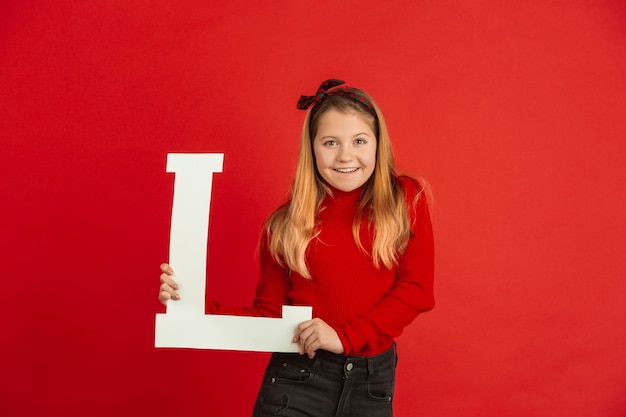 Celebração do dia dos namorados, feliz, linda garota caucasiana segurando a carta no fundo vermelho do estúdio.