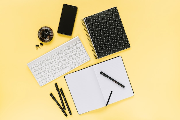 Celular e teclado branco com artigos de papelaria do escritório no fundo amarelo