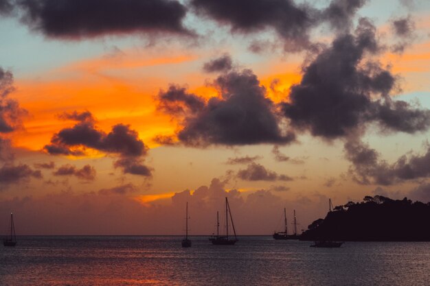 Cenário do pôr do sol com silhueta de montanha e barcos no mar