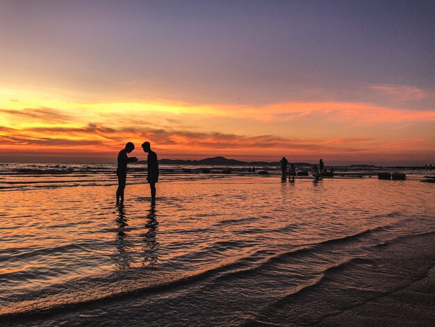 Cenário do pôr do sol com uma silhueta de pessoas na praia