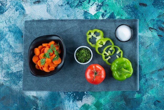 Cenouras fatiadas em uma tigela ao lado de vegetais na toalha em azul.