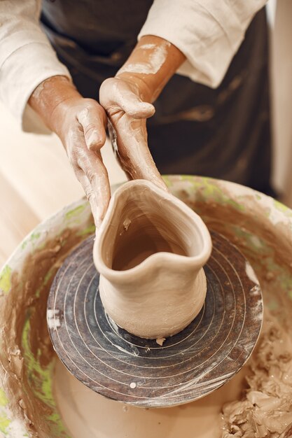 Cerâmica feminina trabalhando com argila na roda em estúdio. Barro com água respingou em torno da roda de oleiro.