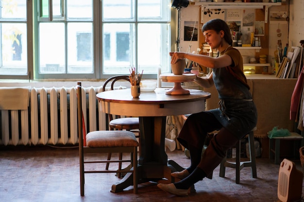 Ceramista em vaso de moldagem de avental na master class em estúdio jovem proprietária de estúdio de cerâmica no trabalho