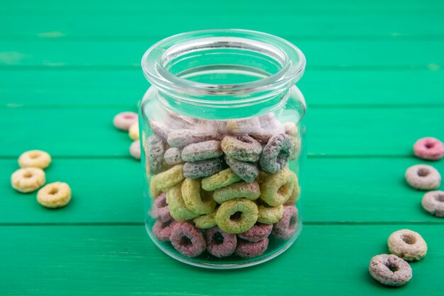 Cereais multicoloridos em uma jarra de vidro com cereais isolados na superfície verde