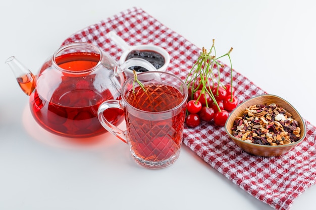 Cereja com chá, geléia, ervas secas, vista de alto ângulo em branco e toalha de cozinha