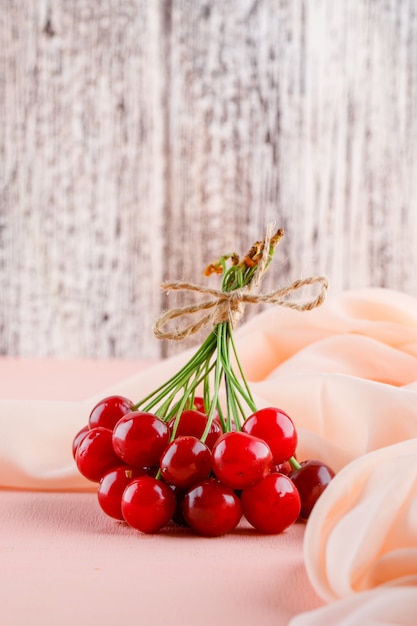 Foto grátis cerejas com vista lateral para têxteis na mesa-de-rosa