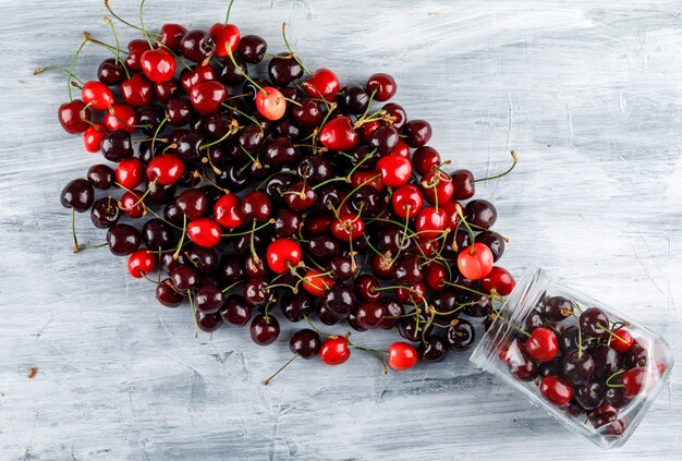 Cerejas dispersas de uma vista superior do frasco em uma superfície de grunge