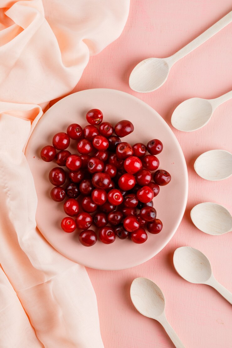 Foto grátis cerejas em um prato com colheres de pau, vista superior em têxteis e rosa