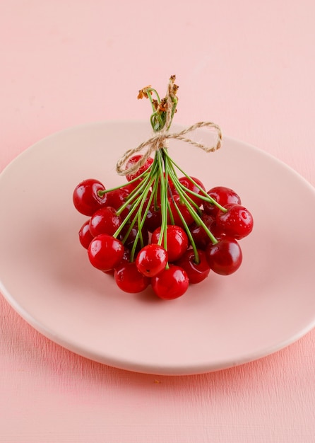 Cerejas em um prato em uma mesa-de-rosa. vista de alto ângulo.