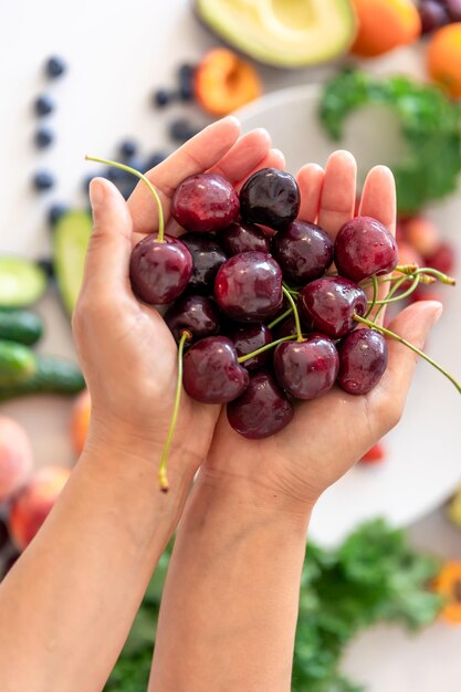 Foto grátis cerejas maduras em mãos de fêmeas em um fundo desfocado de legumes e frutas