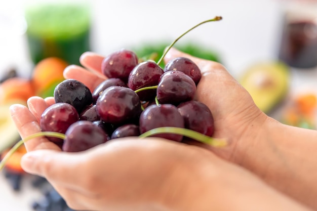 Cerejas maduras em mãos femininas em um fundo desfocado de frutas e legumes