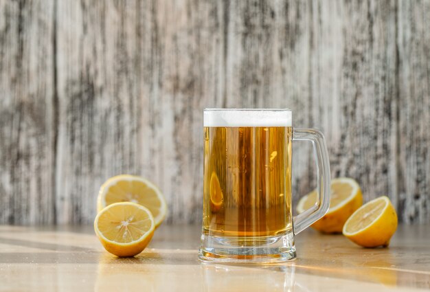 Cerveja com fatias de limão em uma caneca de vidro na mesa suja e leve, vista lateral.