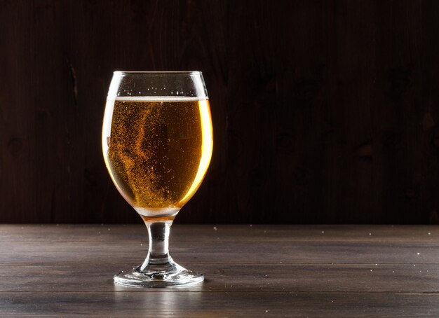 Cerveja em uma vista lateral de vidro de cálice em uma mesa de madeira