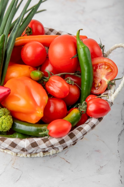 Cesta cheia de legumes como tomate, pimentão e cebolinha na superfície branca