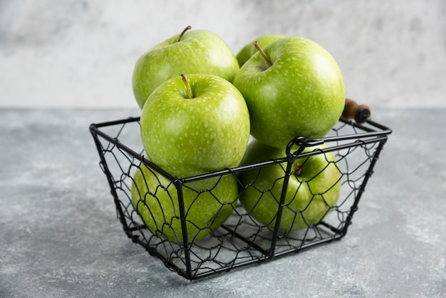 Cesta cheia de maçãs verdes brilhantes na mesa de mármore.