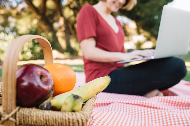 Cesta com frutas perto de mulher com laptop