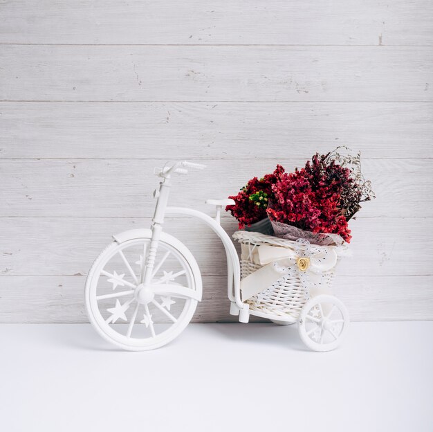 Cesta de flores na bicicleta branca na mesa contra a parede de madeira