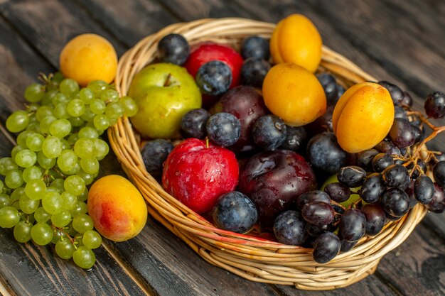 Cesta de meia vista com frutas maduras e frutas ácidas, como uvas, damascos, ameixas na mesa marrom