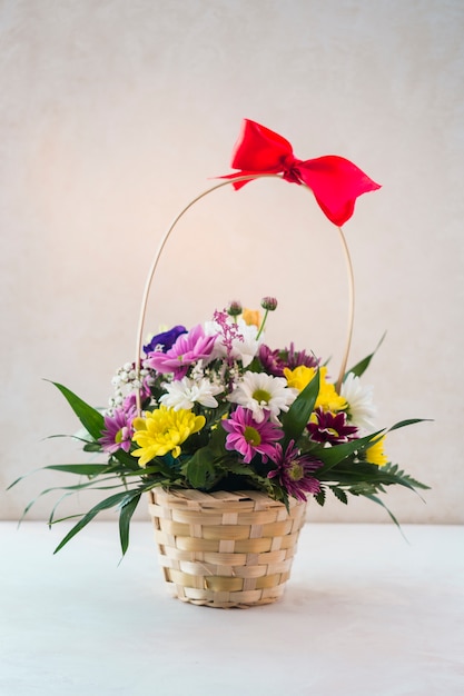 Foto grátis cesta floral com laço vermelho na mesa branca