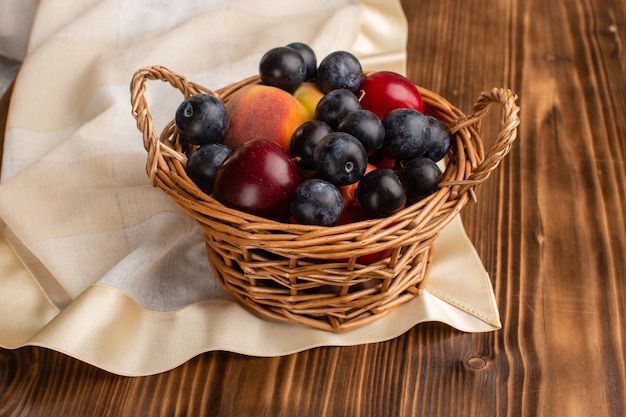 Cesto com frutis ameixas e pêssegos na madeira