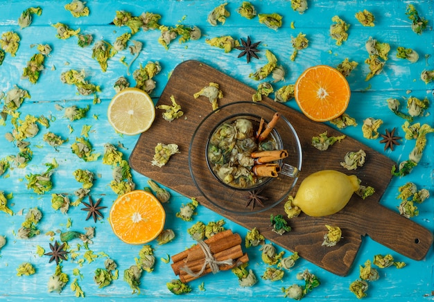 Chá com especiarias, laranja, limão, ervas secas em uma caneca azul e tábua de cortar, vista superior.