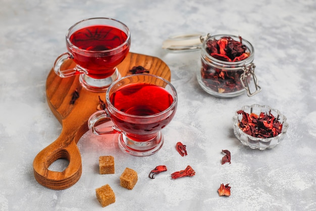 Chá de hibisco vermelho quente em uma caneca de vidro em concreto com pétalas de hibisco seco