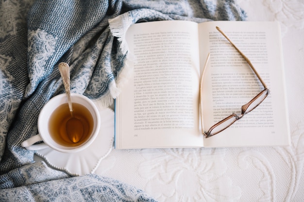 Chá e livro com óculos na cama