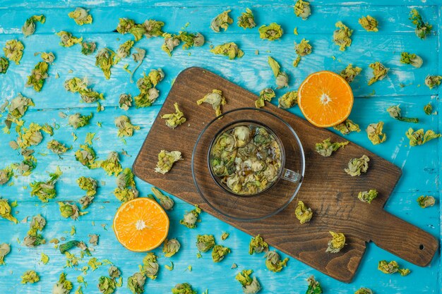 Chá em uma caneca de vidro com laranja, ervas secas, vista superior em azul e tábua de cortar