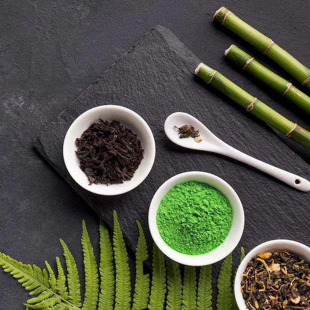 Foto grátis chá matcha verde e erva de chá seco com vara de bambu sobre fundo preto de pedra