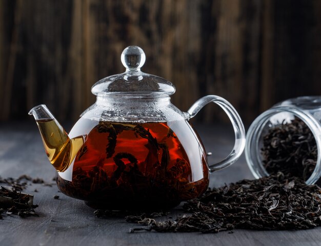 Chá preto com chá seco em um bule de chá na superfície de madeira, vista lateral