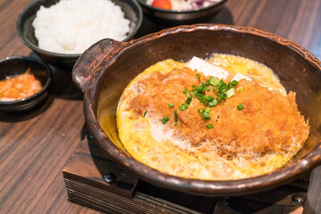 Chaleira de carne de porco fritada em japonês (tonkatsu) coberta com ovo em arroz cozido no vapor.