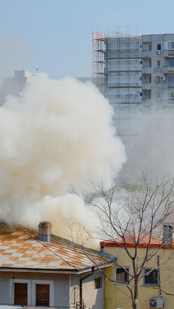 Chamas saindo de casa em chamas no bairro. Fumaça emergindo do telhado em chamas na paisagem da cidade. Fumos perigosos e poluição atmosférica da explosão saindo do prédio destruído