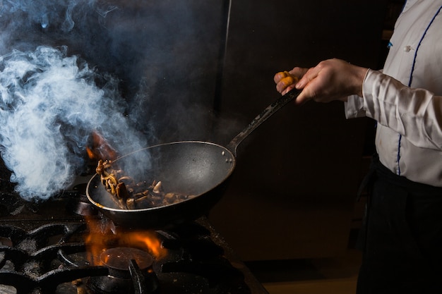 Champignon de vista lateral fritando com fumaça e fogo e humanos no fogão