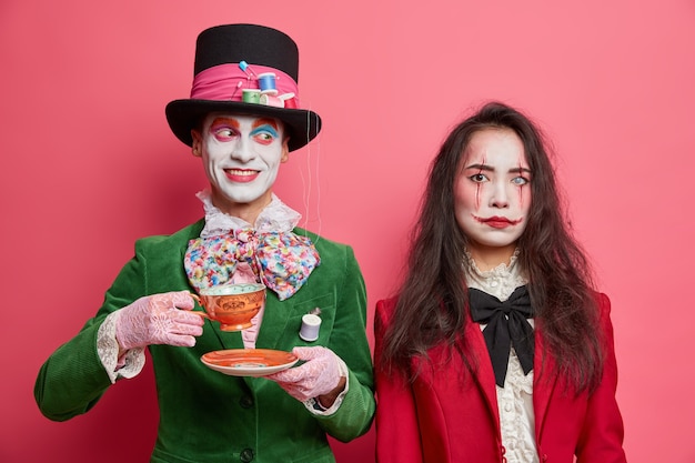 Chapeleiro masculino alegre do país das maravilhas gosta de beber chá na festa e usa um grande chapéu e jaqueta verde. demônio feminino sério com olho de monstro e cicatrizes de sangue