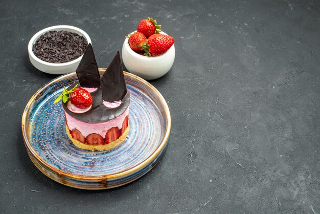 Cheesecake delicioso de vista frontal com morango e chocolate em tigelas de prato com chocolate de morangos no fundo escuro isolado com local de cópia