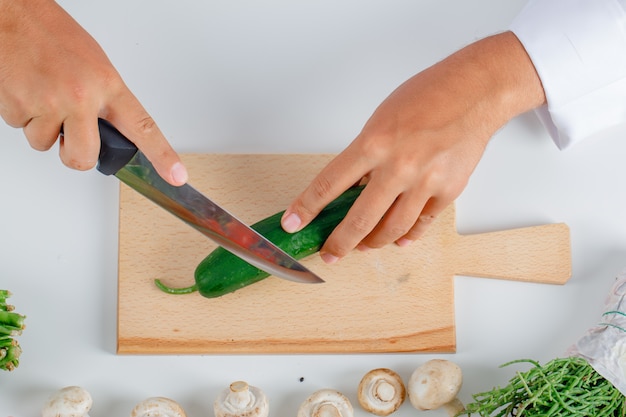 Chef em pepino de corte uniforme na placa de madeira na cozinha