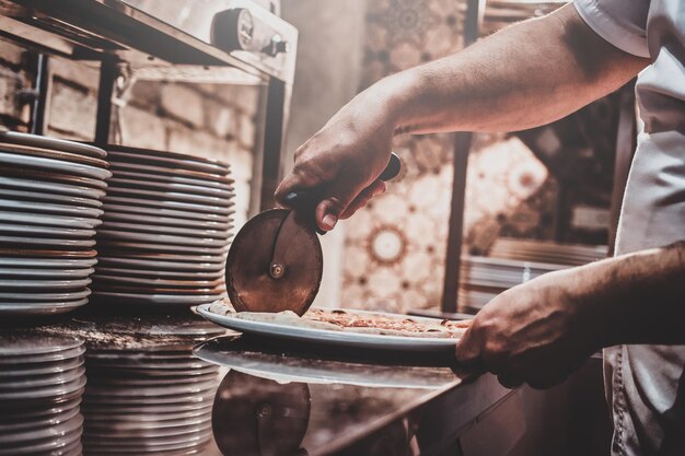 Chef experiente está cortando pizza preparada na hora com faca especial.