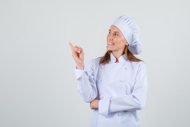 Chef feminina apontando para o lado enquanto olha para o lado com uniforme branco e parece alegre