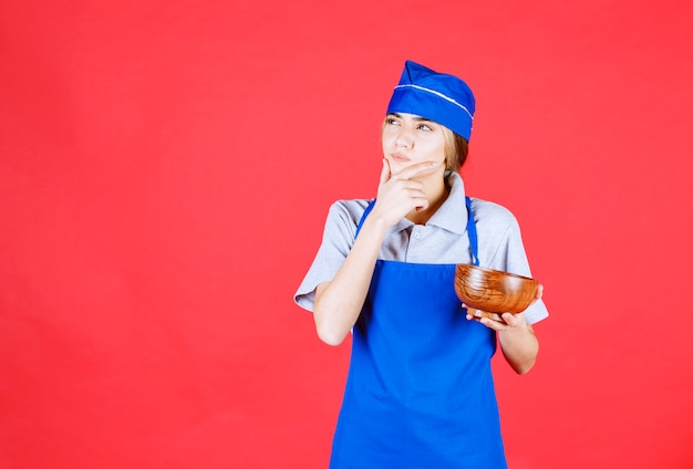 Chef feminina com avental azul segurando uma xícara de macarrão chinês de cobre e pensando