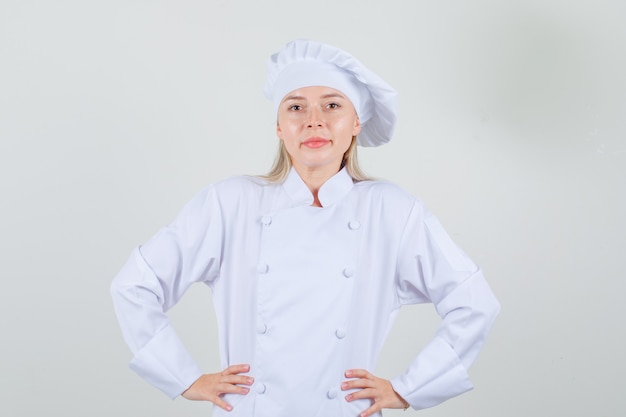 Chef feminina de mãos dadas na cintura e sorrindo em uniforme branco