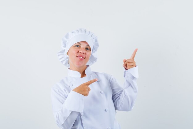 Chef feminina de uniforme branco apontando para o canto superior direito e parecendo confiante