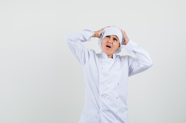 Chef feminina de uniforme branco com as mãos na cabeça e parecendo melancólica