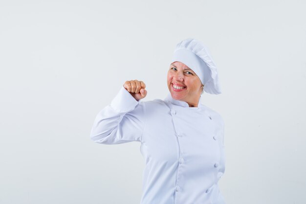 Chef feminina de uniforme branco mostrando gesto de vencedor e parecendo feliz