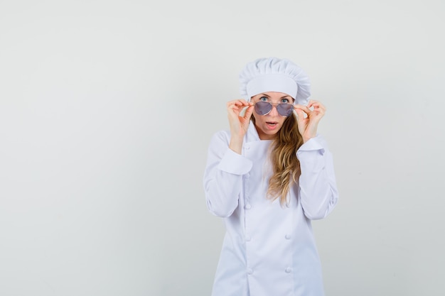 Foto grátis chef feminina de uniforme branco olhando para a câmera por cima dos óculos e parecendo chocada