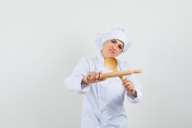 Chef feminina de uniforme branco segurando o rolo e a colher de pau e parecendo confiante