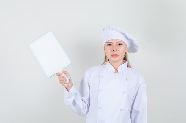 Chef feminina de uniforme branco segurando uma tábua e sorrindo