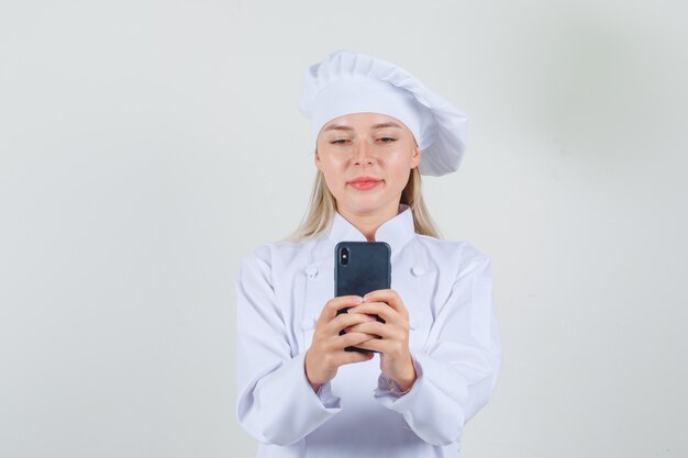 Chef feminina digitando no smartphone e sorrindo em uniforme branco