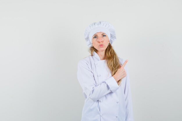 Chef feminina em uniforme branco apontando para longe e fazendo beicinho