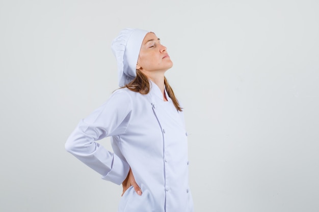 Chef feminina em uniforme branco, sofrendo de dores nas costas e parecendo cansada.