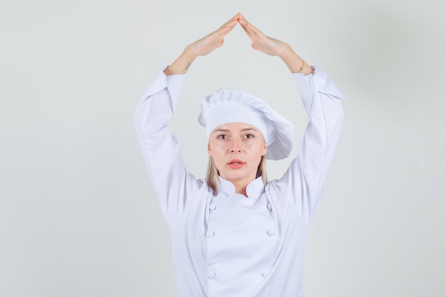 Chef feminina segurando as mãos na cabeça como telhado da casa em uniforme branco